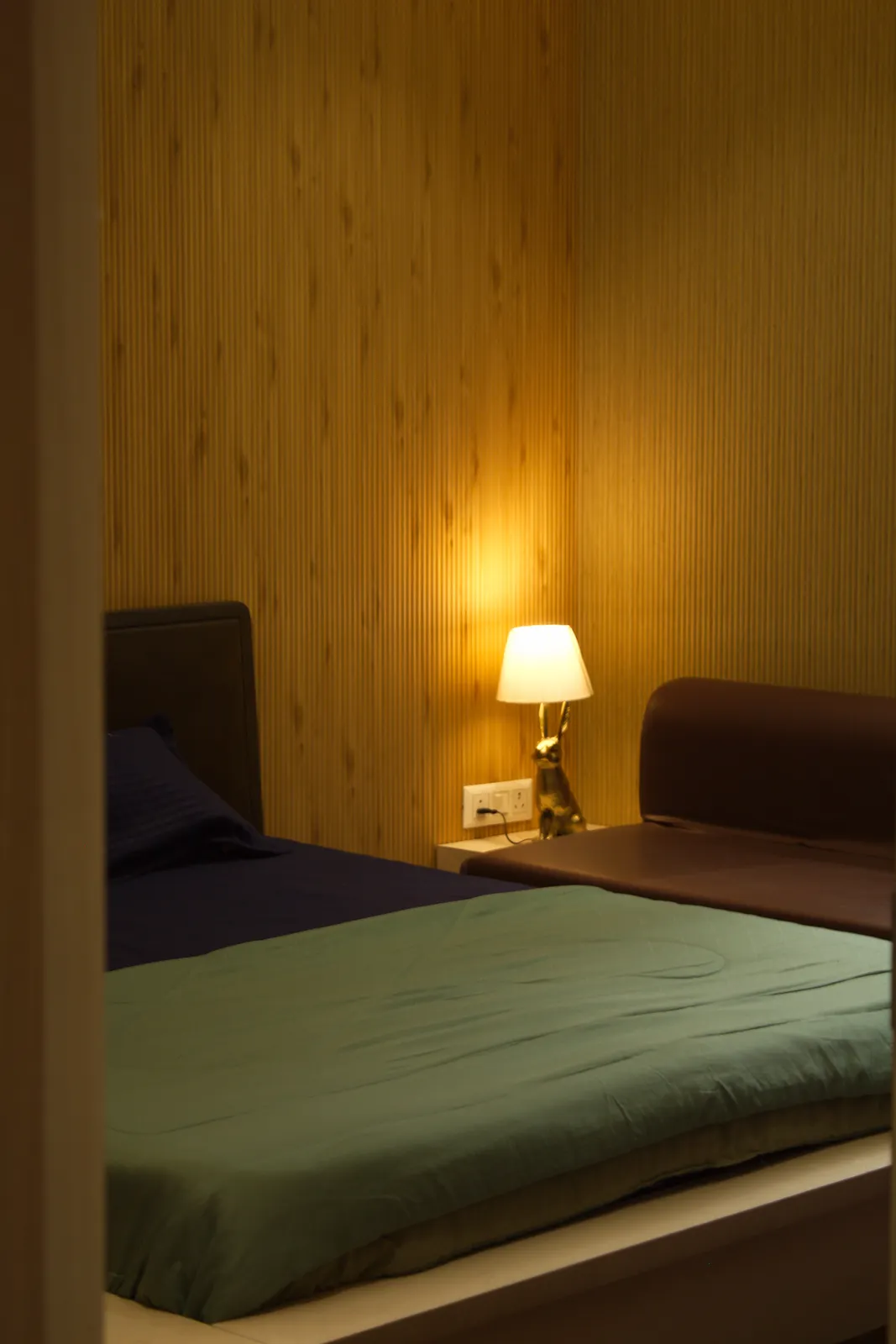 A bedroom in the farmhouse at Raj Organic Farm, with a bedside lamp and a green bedspread