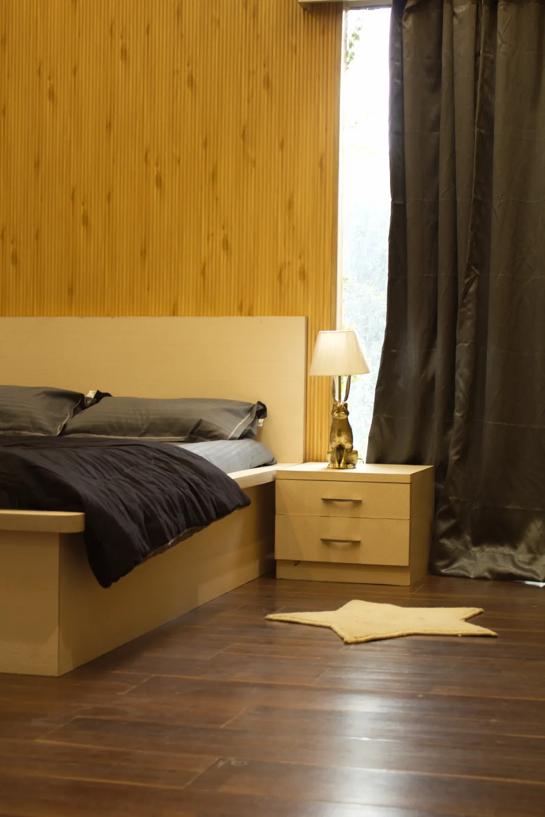 A bedroom in the farmhouse at Raj Organic Farm, with a low double bed, grey curtains and a lamp